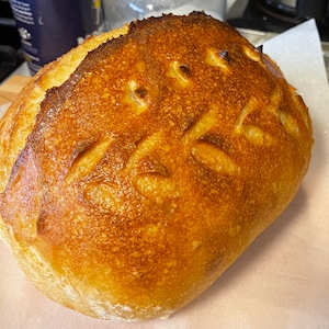 Op de afbeelding: Een goudbruin brood met een knapperige korst en een patroon van insnijdingen op de bovenkant.
