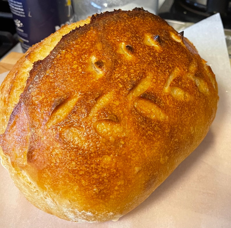 Op de afbeelding: Een goudbruin brood met een knapperige korst en een patroon van insnijdingen op de bovenkant.