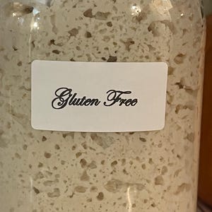 May include: A glass jar filled with a white, bubbly substance. A white label on the jar reads "Gluten Free".