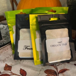 May include: Three small, resealable bags filled with a white powder. The bags are labeled "Fran", "N", and "1847 OREGON TRAIL".