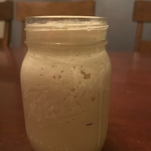 May include: A clear glass jar filled with a light brown, foamy liquid. The jar has a textured surface and a label that is partially visible.