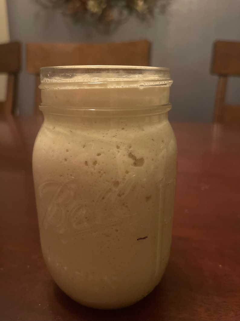 May include: A clear glass jar filled with a light brown, foamy liquid. The jar has a textured surface and a label that is partially visible.