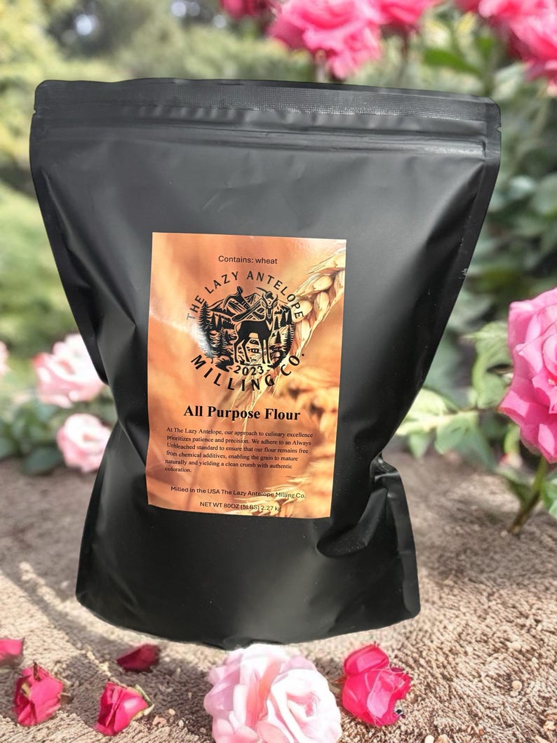 Pu&ograve; includere: Un sacco nero di "Farina per tutti gli usi" di The Lazy Antelope Milling Co. La borsa ha un'etichetta marrone con testo e una grafica di un'antilope. La borsa contiene 227g di farina.