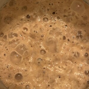 May include: Close-up of a brown sourdough starter with a bubbly, foamy texture.