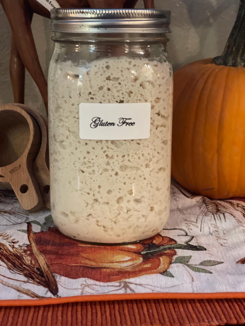 May include: A glass jar filled with a white, bubbly substance labeled "Gluten Free". The jar is sitting on a table with a white tablecloth with a pumpkin design.