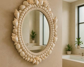 May include: Oval-shaped mirror with a cream-colored frame adorned with various seashells. The mirror is mounted on a beige tiled wall, reflecting a bathroom interior. The frame is decorated with different sizes and shapes of seashells.