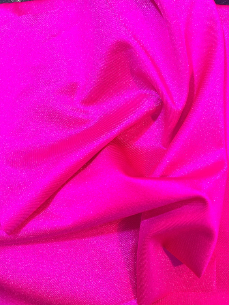 May include: A close-up of a bright pink fabric with a subtle shimmer. The fabric is wrinkled and has a soft, smooth texture.