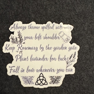 May include: A white sticker with a black and purple design. The sticker features a quote about superstition and luck: "Always throw spilled salt over your left shoulder. Keep Rosemary by the garden gate. Plant lavender for luck. Fall in love whenever you can."