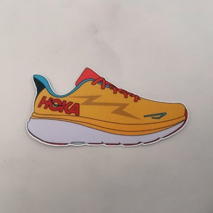 May include: A sticker of a yellow running shoe with red laces and the word "HOKA" in red. The shoe has a white sole and a blue accent on the heel. Lightning bolt graphics are on the side.
