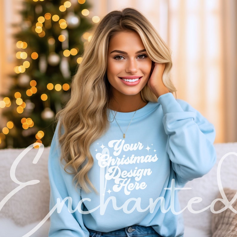 Może przedstawiać: Jasno błękitna bluza z napisem "Your Christmas Design Here" w kolorze białym. Bluzę nosi osoba z długimi blond włosami.