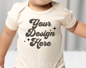 May include: A cream-colored baby onesie with short sleeves and the text "Your Design Here" in brown with a retro font and small star accents.
