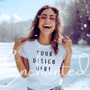 May include: White t-shirt with the text "YOUR DESIGN HERE" in black. The person is smiling and wearing the t-shirt in a snowy outdoor setting. The word "Enchanted" is written in a cursive font across the image.