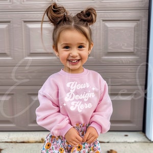 May include: A young girl wearing a pink sweatshirt with the text "Your Design Here" in white. She is smiling and has her hair in two buns.