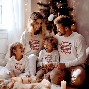 Op de afbeelding: Een gezin van vier personen draagt witte shirts met lange mouwen met een rood-wit kerstontwerp met de tekst "Your Christmas Design Here". Het gezin zit voor een kerstboom.