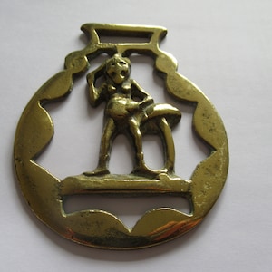 Puede incluir: Un latón de caballo de latón con un diseño detallado de una persona sosteniendo un hongo. El latón es de color dorado y tiene un aspecto desgastado.