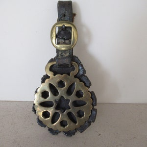 May include: A brass horse brass with a decorative floral design, attached to a leather strap with a brass buckle.