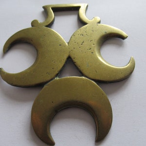 Könnte beinhalten: Ein Messing-Pferde-Anhänger mit einem Design aus drei Halbmonden. Das Messing hat eine goldene Farbe und wirkt abgenutzt und antik.