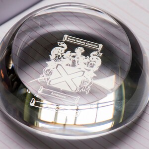 Peut inclure: Un presse-papier en verre transparent avec un design grav&eacute; en argent d'un blason. Le blason pr&eacute;sente une croix, un oiseau et le texte "Victoria Fortuna Experienta" et "Andrews".