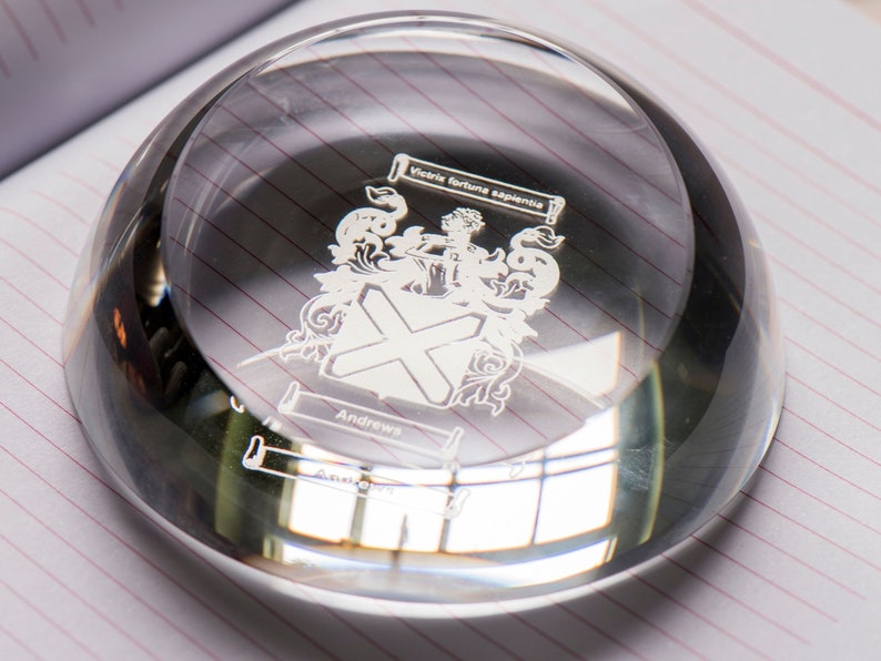 Peut inclure: Un presse-papier en verre transparent avec un design grav&eacute; en argent d'un blason. Le blason pr&eacute;sente une croix, un oiseau et le texte "Victoria Fortuna Experienta" et "Andrews".