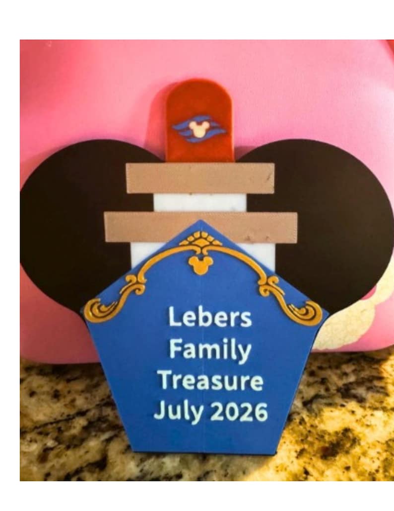 Puede incluir: Un letrero de tesoro familiar azul, dorado y blanco con el texto "Lebers Family Treasure July 2026". El letrero tiene forma de sombrero con orejas de Mickey Mouse y un icono de Mickey Mouse rojo y blanco.