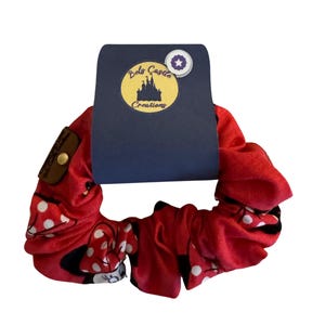 May include: Red scrunchie with a Minnie Mouse print. The scrunchie is tied in a knot and has a blue tag with the text "Bels Castle Creations" and a star.