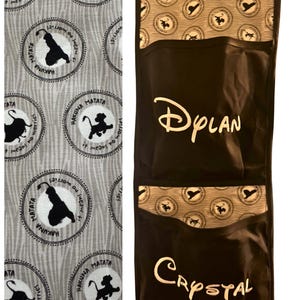 May include: A black and grey hanging organiser with two pockets. The top section features a pattern with the text "Hakuna Matata" and a silhouette of a lion. The pockets are black with the names "Dylan" and "Crystal" in white.