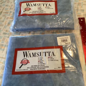 May include: Two packages of Wamsutta brand bed sheets in a light blue color. The packaging includes a red and white label with product details, including thread count and material composition. The sheets are available in various sizes.
