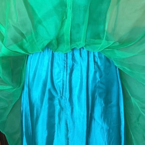 以下が含まれることがあります： 鮮やかな色の組み合わせのツーピースドレス。上層は透け感のある明るい緑色の生地で、下層はターコイズブルーの無地です。流れるようなレイヤードデザインで、特別な機会に適しています。