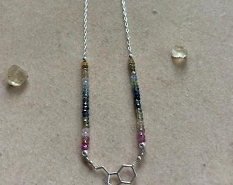 May include: A silver necklace with a colorful gemstone bead chain and a silver serotonin molecule pendant.
