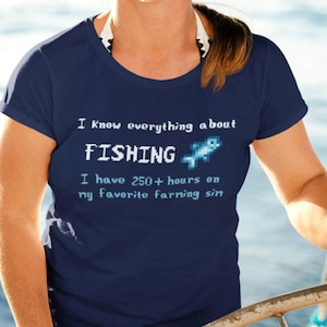 A woman steering a sailboat while wearing a navy blue t-shirt with the phrase "I know everything about fishing – I have 250+ hours on my favorite farming sim" and a pixel art fish. A fun and humorous shirt for gamers who love farming sims and relaxing gameplay, featuring retro-inspired pixel graphics and quirky game humor.