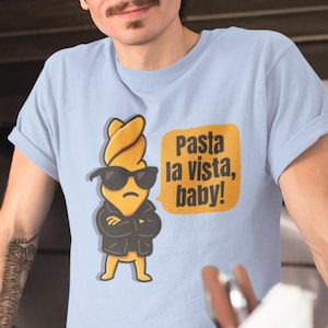 May include: A light blue t-shirt with a cartoon illustration of a pasta noodle wearing sunglasses and a leather jacket. The text "Pasta la vista, baby!" is printed on the shirt.