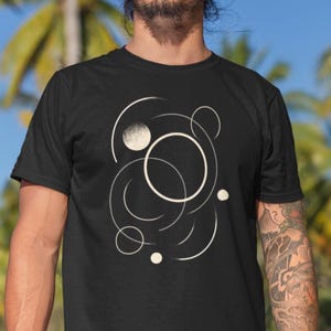 Minimalist geometric t-shirt featuring an elegant beige line art design of interlaced circles and arcs on a black background. The composition evokes motion and balance, creating a modern, artistic look suitable for both men and women.
