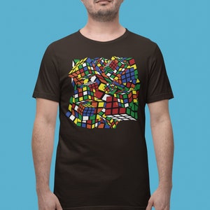 May include: A brown t-shirt with a colorful, abstract design of a Rubik's Cube. The design is made up of various colored squares, creating a 3D effect.