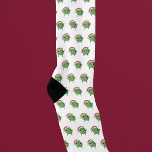 May include: White knee-high socks with a repeating pattern of green cartoon characters wearing Santa hats.