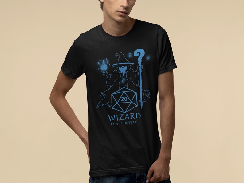 Black wizard shirt featuring a bold blue graphic of a wizard casting a fireball, holding a glowing staff, with a D20 dice showing a natural 20. Includes fantasy-themed text that reads “WIZARD – I CAST FIREBALL” making it a fun gift for tabletop players and DnD fans.
