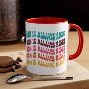 Op de afbeelding: Witte keramische koffiemok met een rode rand en handvat. De mok heeft de tekst "Mom is always right" vijf keer herhaald in een regenboog van kleuren.
