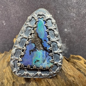 May include: A white ceramic mug with a black handle and the text "But First, Coffee" in a bold, black font. The mug is set against a blurred background, suggesting a cozy setting.