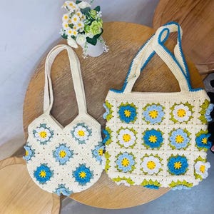 May include: Two crocheted bags with floral designs. The larger bag is rectangular with a blue, green, and white floral pattern. The smaller bag is round with a blue and white floral pattern.