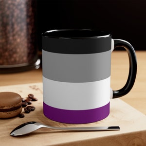 May include: A black coffee mug with a white handle. The mug has a design of the asexual pride flag, which is black, gray, white, and purple.
