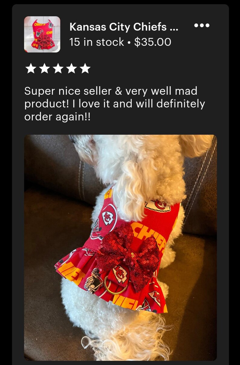 May include: A white dog wearing a red and yellow Kansas City Chiefs dog harness with a red sequined bow. The harness has the team logo and the word "Chiefs" printed on it.
