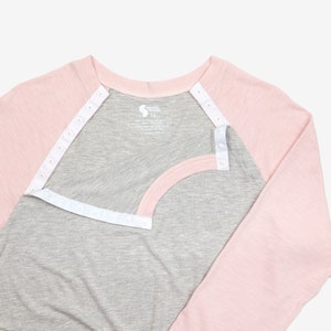 May include: A gray and pink long-sleeved shirt with a white snap closure down the front. The shirt has a baseball style design with a gray body and pink sleeves.