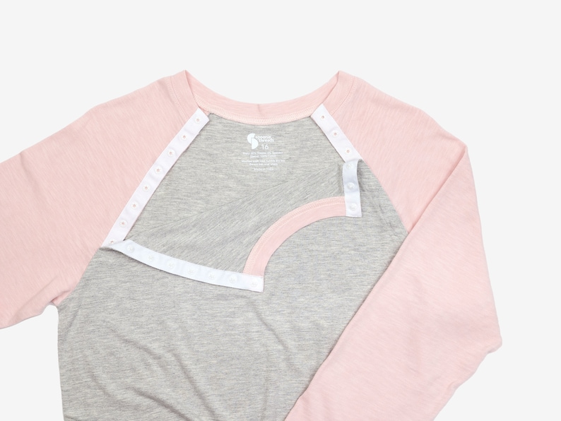 May include: A gray and pink long-sleeved shirt with a white snap closure down the front. The shirt has a baseball style design with a gray body and pink sleeves.