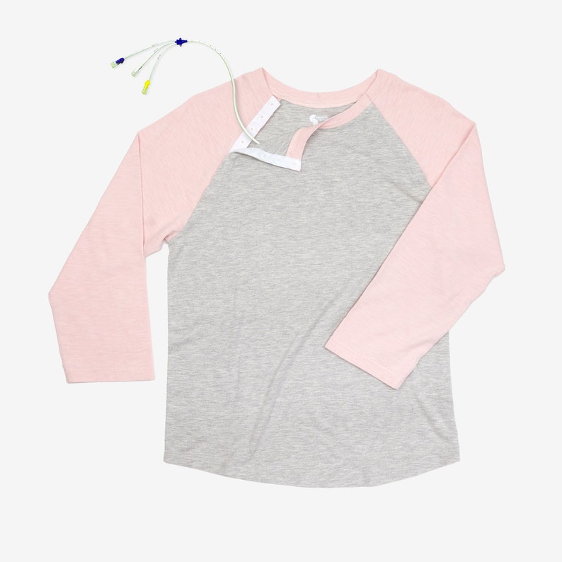 May include: A gray and pink baseball tee shirt with a white snap closure at the neckline. The shirt has a long sleeve on one side and a three-quarter sleeve on the other.