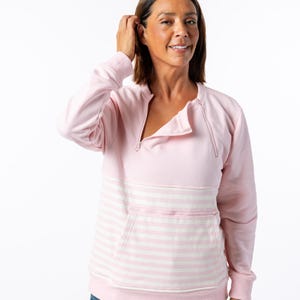 May include: A light pink sweatshirt with a quarter-zip neckline and a kangaroo pocket. The pocket and lower section of the sweatshirt feature horizontal white and pink stripes. The long-sleeved top is made of a soft material.