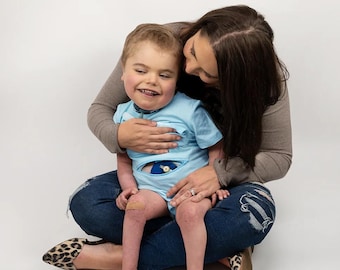 May include: A woman and a young boy are sitting on the floor. The woman is wearing blue jeans and a brown sweater. The boy is wearing a light blue shirt and has a bandage on his knee. They are both smiling.