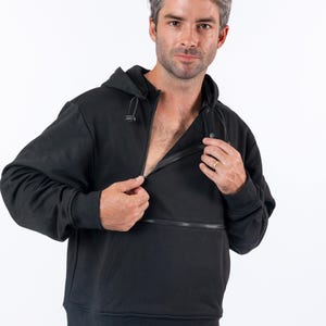 May include: A black hooded sweatshirt featuring a diagonal zipper closure across the chest, a drawstring hood with toggles, long sleeves with ribbed cuffs, and a ribbed hem. The garment is worn over blue denim jeans, showcasing a functional design.