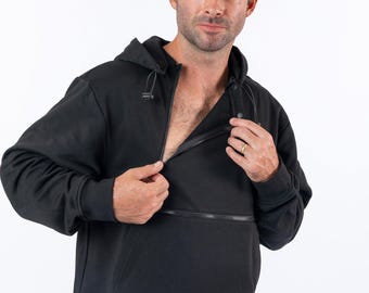 May include: A black hooded sweatshirt featuring a diagonal zipper closure across the chest, a drawstring hood with toggles, long sleeves with ribbed cuffs, and a ribbed hem. The garment is worn over blue denim jeans, showcasing a functional design.