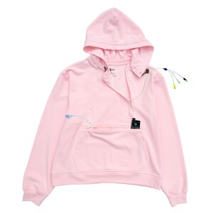 May include: A light pink hoodie with a front zipper, a hood, and a kangaroo pocket. The hoodie has a small black device in the pocket and several wires attached to it.