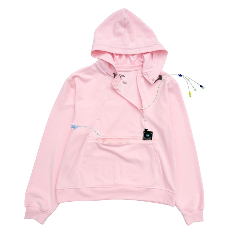 May include: A light pink hoodie with a front zipper, a hood, and a kangaroo pocket. The hoodie has a small black device in the pocket and several wires attached to it.