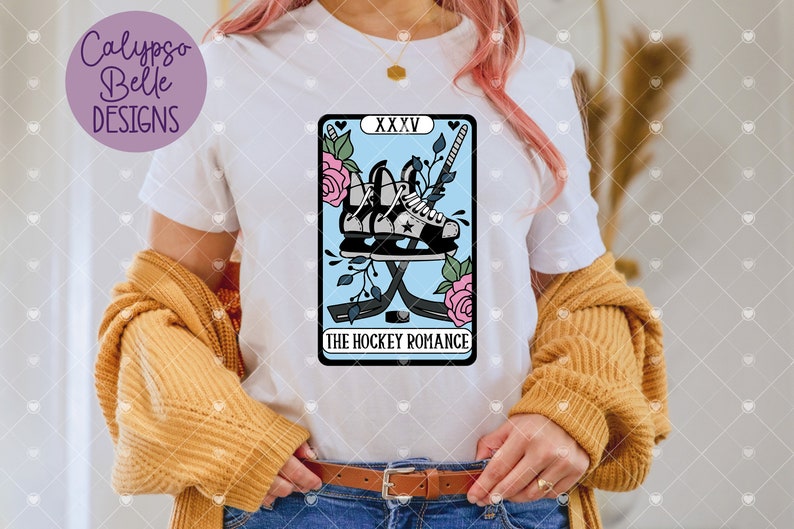 May include: A white t-shirt with a blue and pink tarot card design featuring a pair of hockey skates and sticks with the text "The Hockey Romance" and "XXXV".